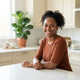 Portrait of a smiling woman in a bright, modern kitchen with forest green and cream decor.